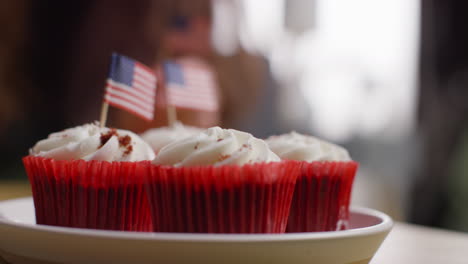 Close-Up-Of-Woman-At-Home-Putting-Miniature-American-Stars-And-Stripes-Flags-Into-Cupcakes-For-Party-Celebrating-4th-July-Independence-Day