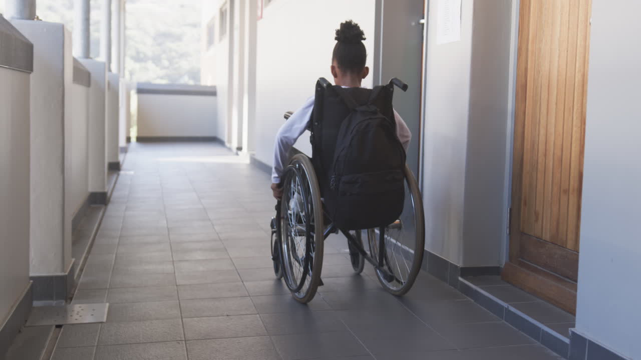 In school, student in wheelchair moving through hallway, carrying backpack