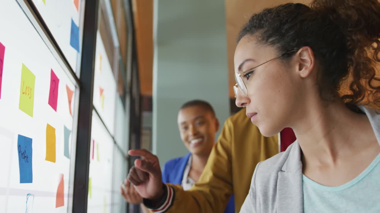 Happy diverse male and female creative colleagues writing on memo notes, brainstorming on glass wall