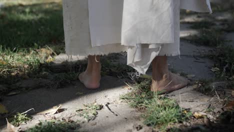 A-man-wearing-a-white,-tattered-robe-and-dressed-as-Jesus-Christ-stands-in-slow-motion-on-a-sidewalk