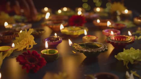 Primer-Plano-De-Manos-Encendiendo-Lámparas-De-Aceite-Diya-Celebrando-El-Festival-De-Diwali-En-Una-Mesa-Oscura