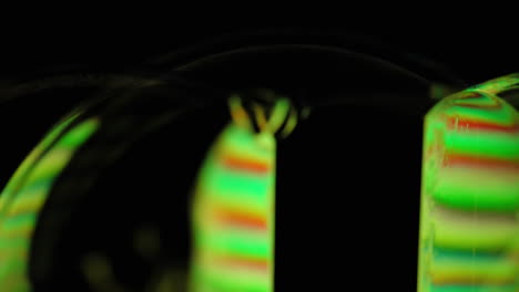 Dramatic-close-up-of-green-and-orange-light-refracting-through-and-reflecting-on-spinning-soap-bubbles-on-black-background,-macro