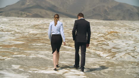 Tired-Business-People-Walking-In-Arid-Desert-Towards-Mountains