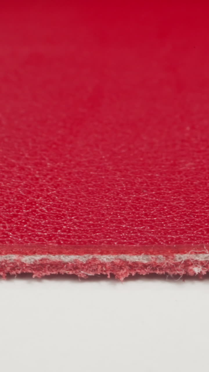 Seam on edge of red color cow leather material on white cutting table macro view. Material sheet in sewing workshop. Design ideas and decorative techniques