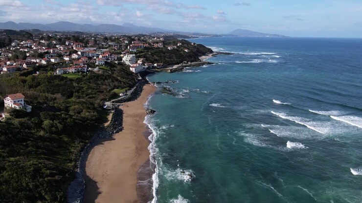 Vista della costa del Paese Basco francese da Bidart Parlamentia Surf Break a Guethary e fino alla Spagna, con le onde che si infrangono sotto e le montagne sullo sfondo.