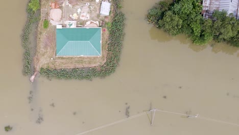 a rural house stands amid floodwaters with electric poles partially submerged in sylhet, bangladesh, south asia - aerial descend shot