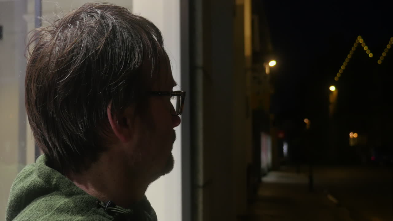Caucasian man waiting outside quiet street shop window in the late cold night air, side view