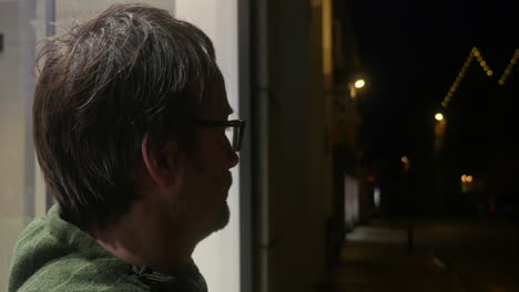 hombre caucásico esperando fuera de la ventana de la calle tranquila en el aire frío de la noche, vista lateral