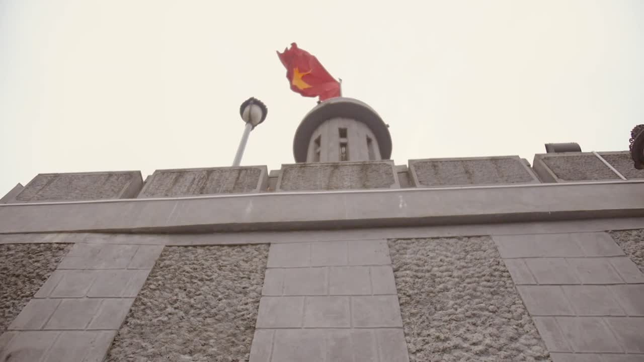 looking up to Lũng Cú Flag Tower behind wall with Vietnamese flag fluttering in the wind