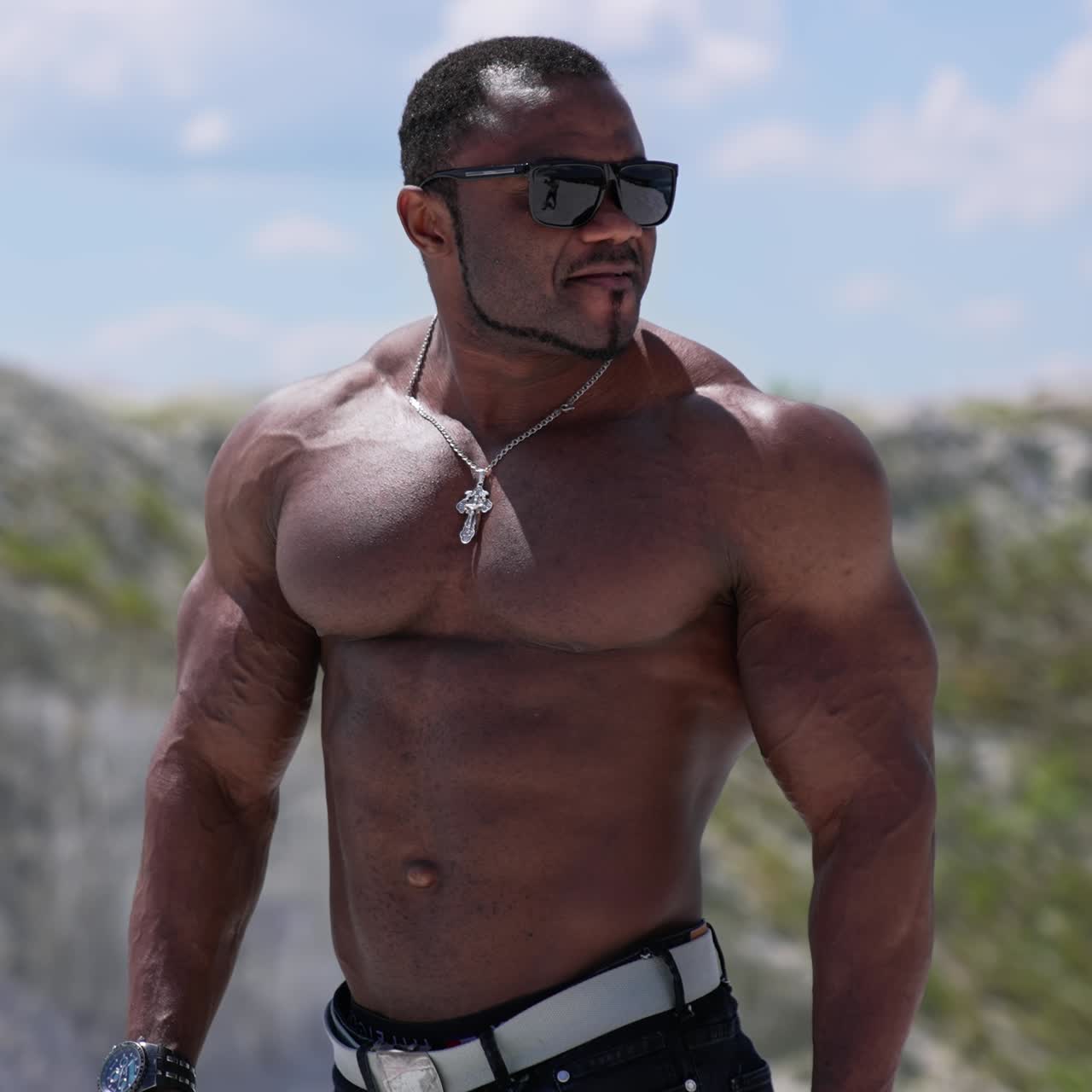 Waist up portrait view of the athletic naked man wearing glasses walking outside and showing his naked torso. Man posing at the sandy beach