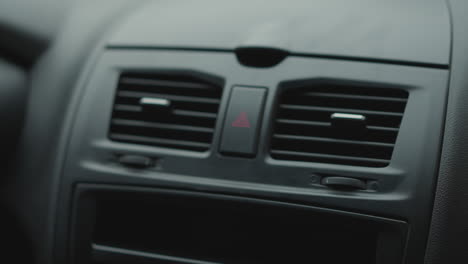 close up of male hand tapping air conditioner vent control button on car dashboard focusing on finger gesture ambient cabin lighting textured vent slats and control panel detail during winter commute