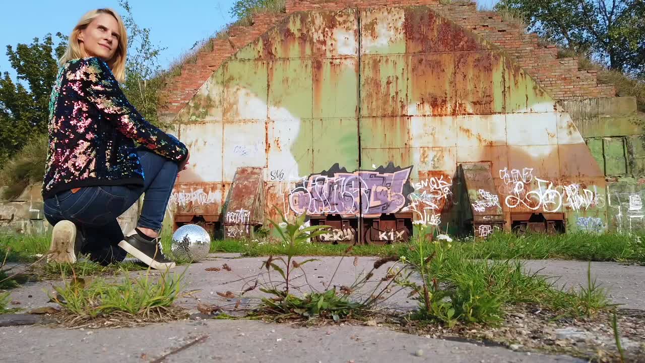 Perfetta ripresa cinematografica in slow motion dietro le quinte di una ragazza bionda che fa il segno della pace su un hangar di aerei russo e una sfera a specchi. Servizio fotografico e video in luoghi abbandonati nella natura 1080, 24p di Philipp Marnitz