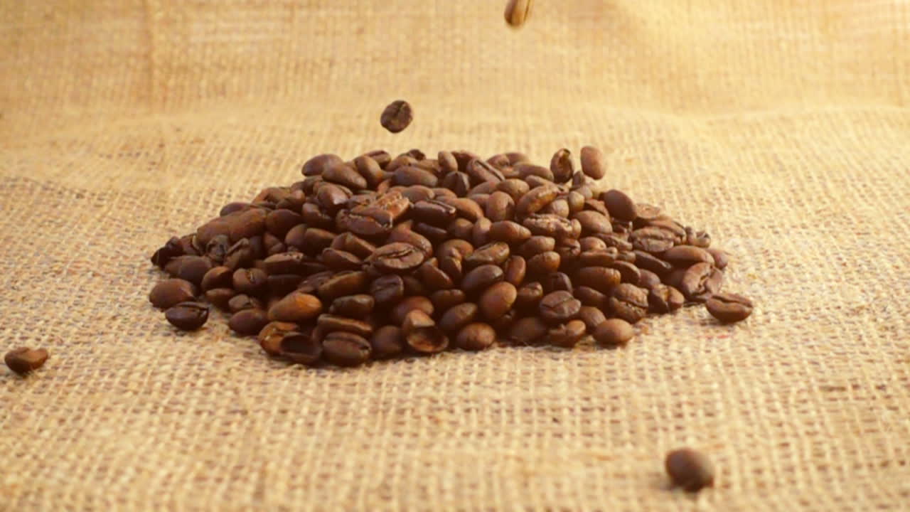 Chicchi di caffè cadono su tela di iuta al rallentatore.