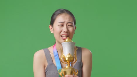 close up of asian woman with a gold medal singing on a gold trophy celebrating winning as the first winner on green screen background in the studio