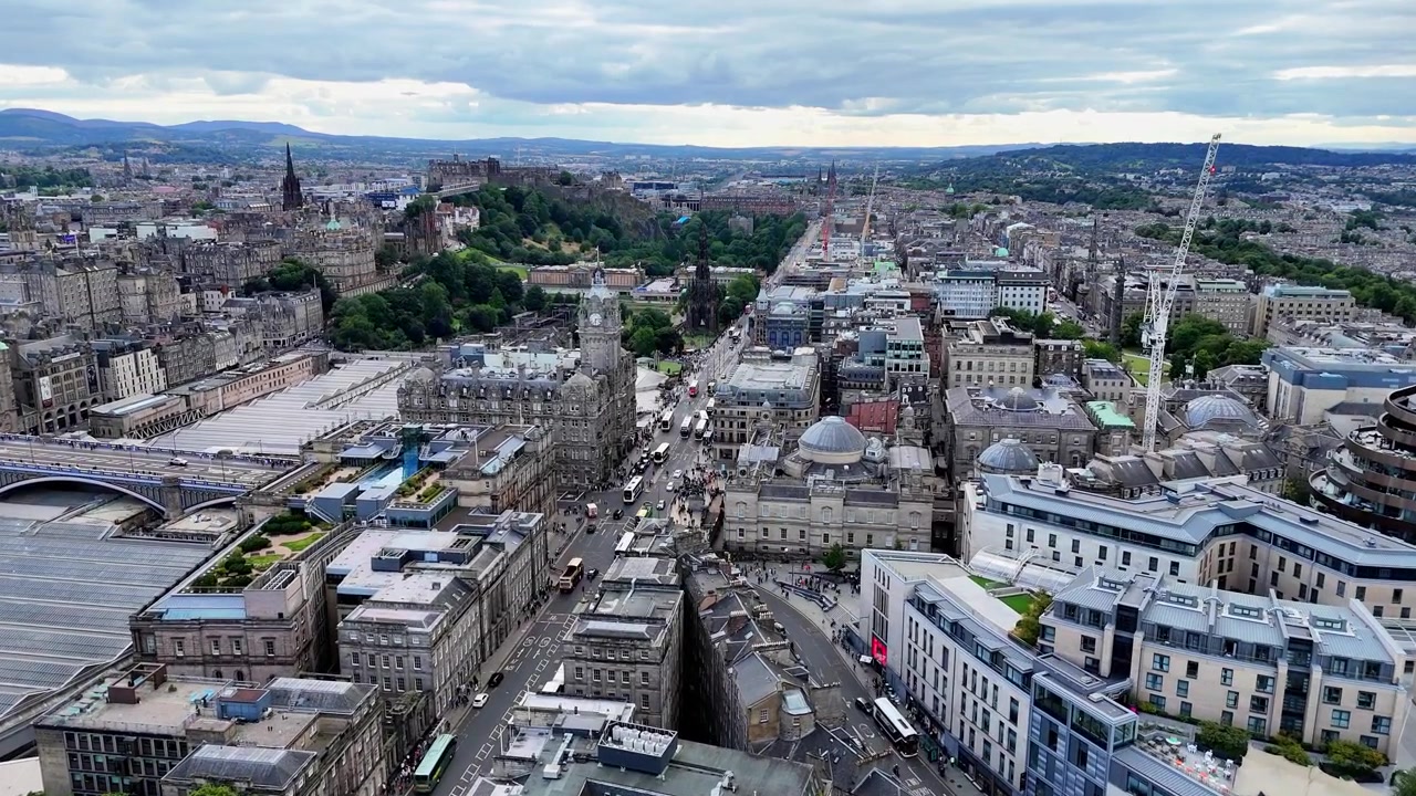 Sobrevoo aéreo da Princes Street com o Castelo de Edimburgo e o horizonte histórico da cidade. Escócia.