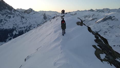 Drohnenaufnahmen-Von-Drei-Personen,-Die-Sich-Umdrehen-Und-Mit-Schneeschuhen-Auf-Einem-Schneebedeckten-Bergrücken-In-Der-Nähe-Des-Pic-Du-Midi-D&#39;Ossau-Laufen