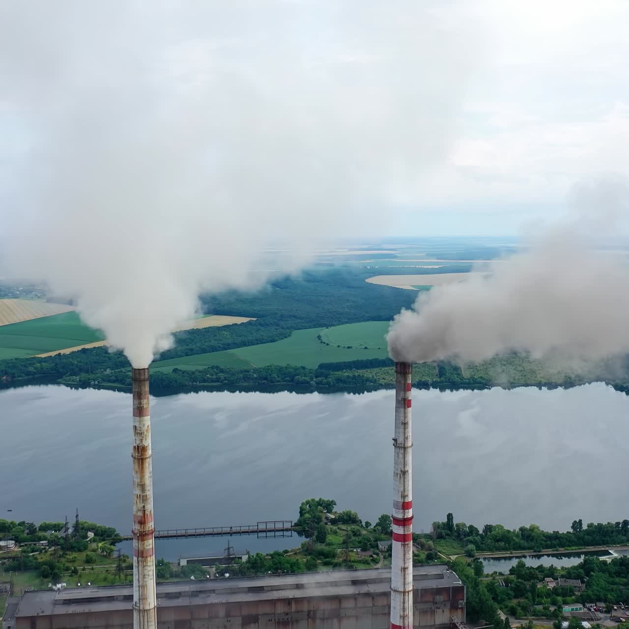 White stack of smoke coming out from large chimneys. Factory chimneys releases harmful emissions into the atmosphere on nature backdrop.Environmental problems