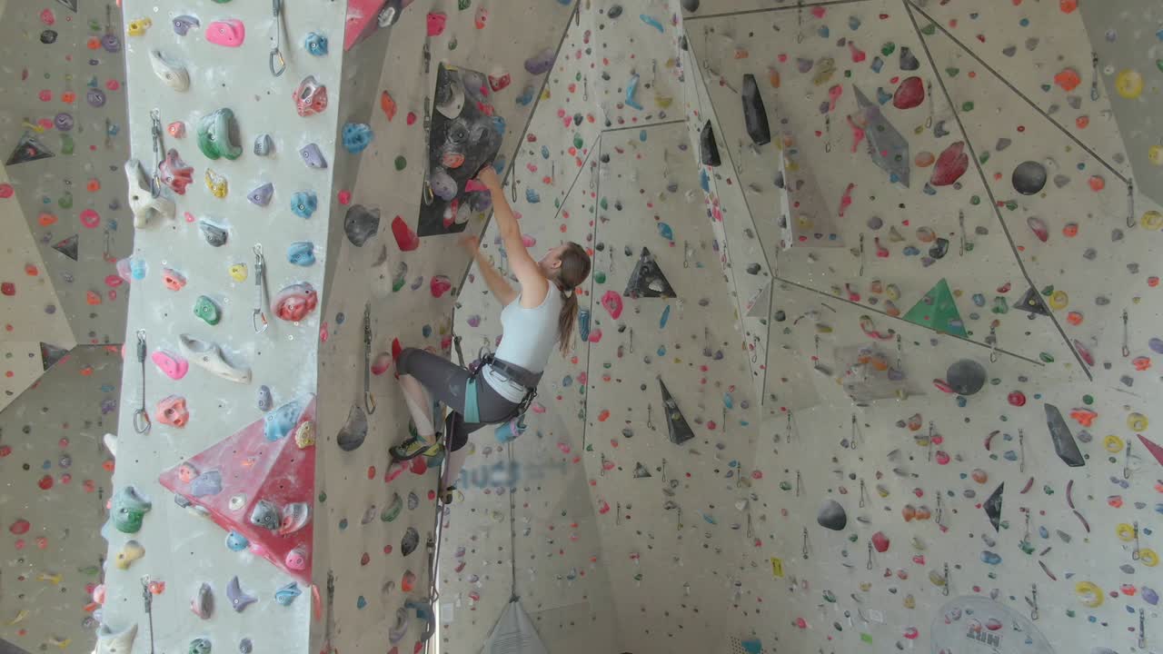 drone: joven escaladora de roca escalando en un centro de entrenamiento interior fresco.