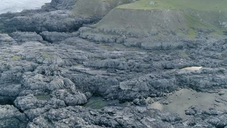 Seguimiento-Aéreo-Sobre-Una-Gran-Franja-De-Costa-Rocosa-Con-Riscos,-Ensenadas,-Cuevas-Y-Pozas-De-Roca-Antes-De-Seguir-Adelante-Sobre-La-Costa-Montañosa-Cubierta-De-Hierba