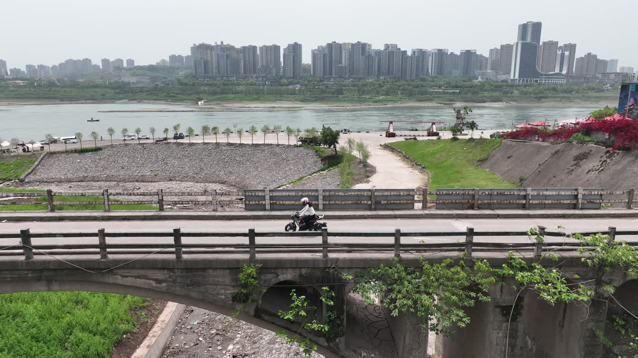 There is a female rider riding a motorcycle on an ancient bridge