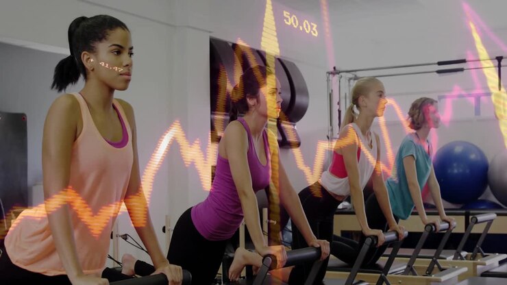 Pilates group adjusting knee pads, gripping bars, pushing carriage with synced waveform toning core