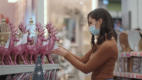 a woman in a protective mask chooses christmas decorations. preparing for christmas in the coronavirus pandemic. christmas tree toys