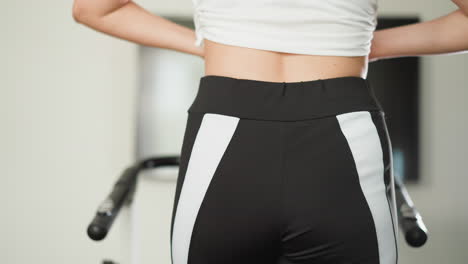 woman adjusts top for training at home closeup. slim lady wearing comfortable activewear exercises on treadmill in domestic gym slow motion. active lifestyle