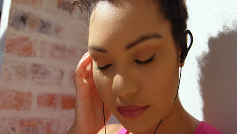 Front-view-of-young-mixed-race-woman-leaning-against-the-wall-in-backyard-of-home-4k