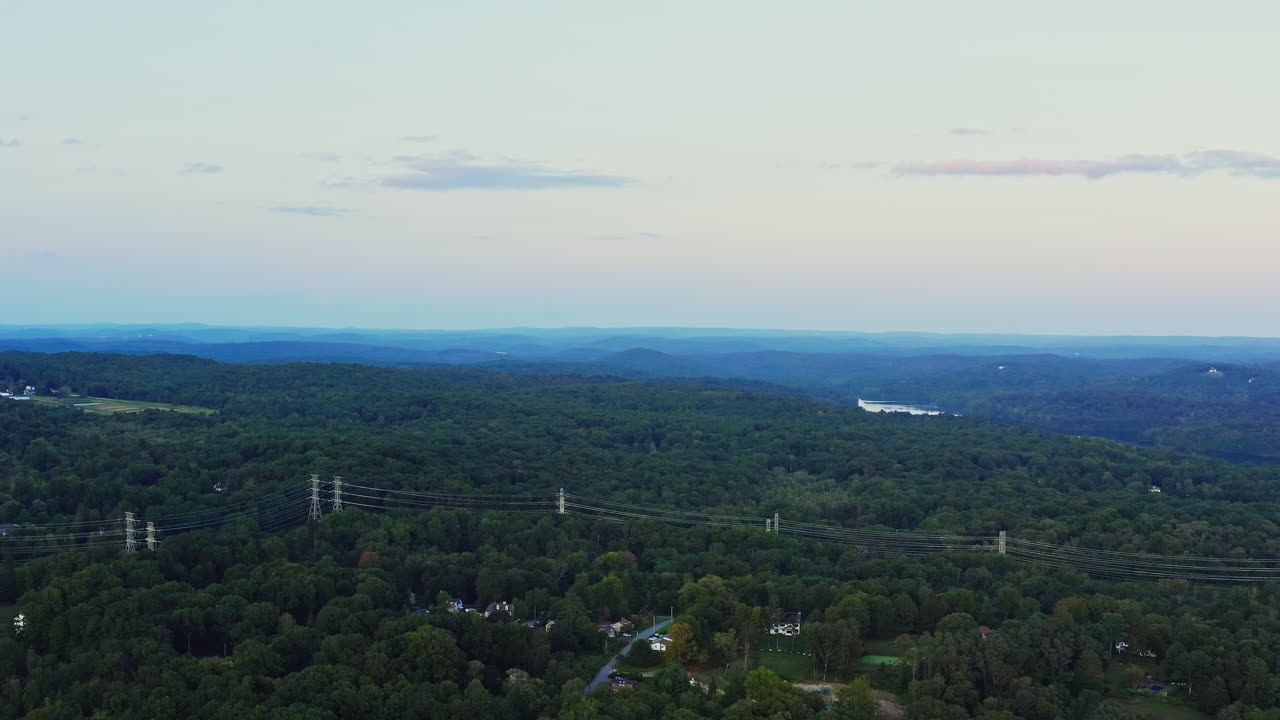 Drone fly-in capturing the expansive forests, rolling hills, and residential pockets of Yorktown Heights, NY. Scenic view with serene pastel skies at dusk.