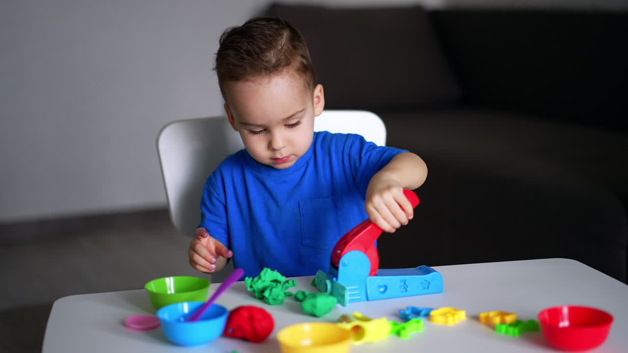 Charming Caucasian toddler playing with plasticine. Little kid is using special machine to squeeze the plasticine for sculpturing.