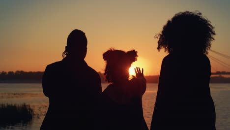 ontspannend familie silhouet samen staan aan de oever van de rivier bij gouden zonsondergang.