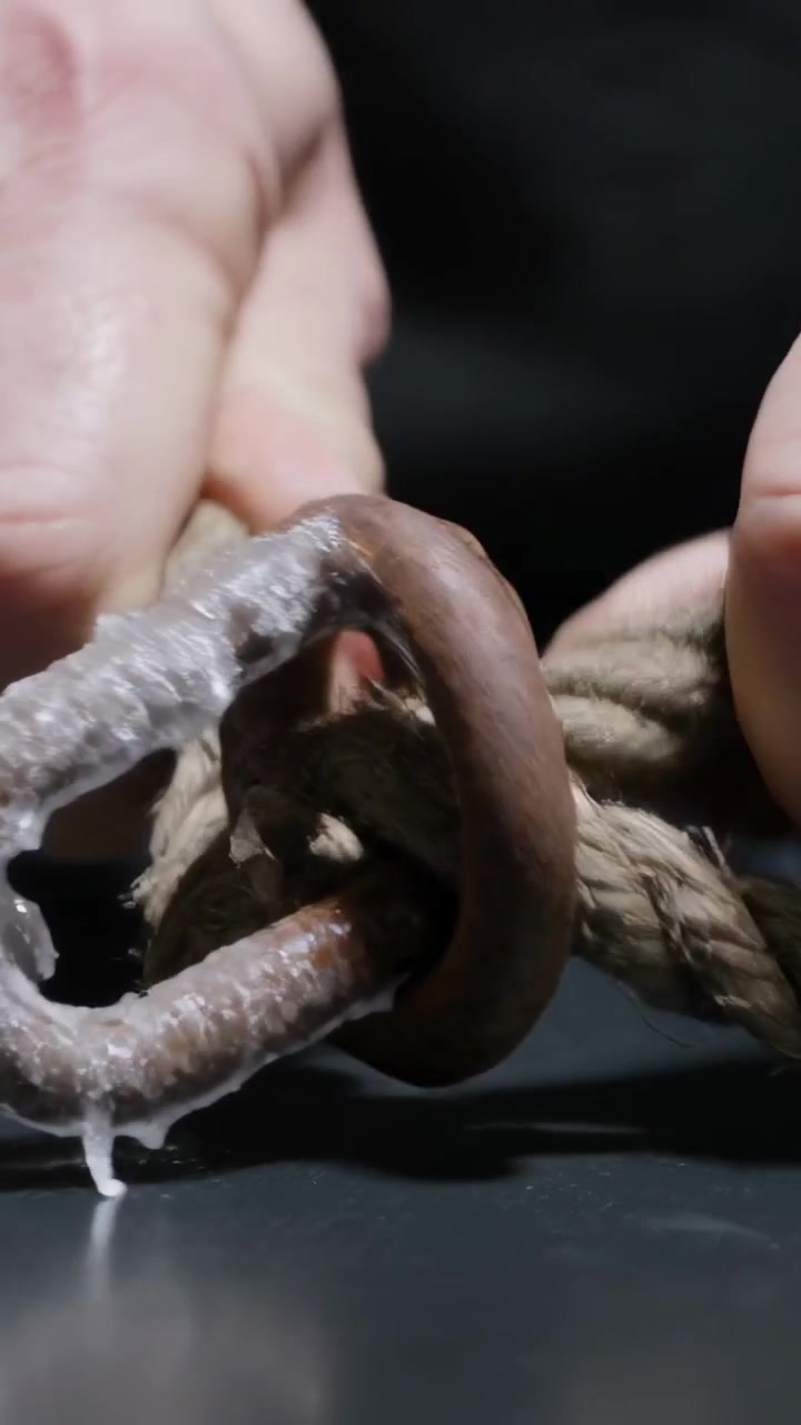Video verticale: Mani nude che infilano una corda attraverso un anello ghiacciato su una panchina, causando la caduta di un ghiacciolo.