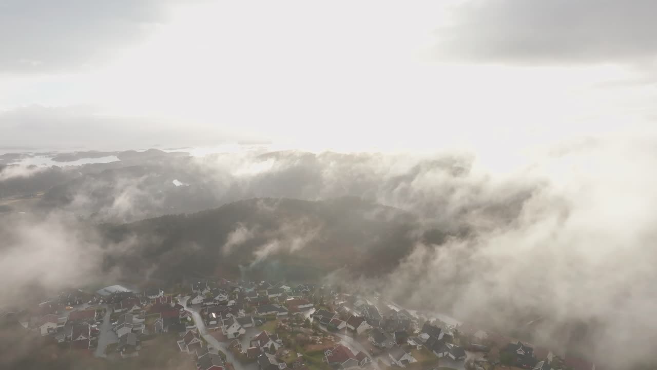 공중에 떠다니는 안개와 구름을 비추는 태양과 함께 노르웨이 주택 단지의 드론 영상