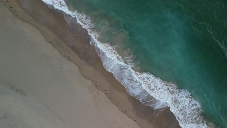 Descending-Aerial-View-Over-a-Pristine-Beach-in-Cornwall-with-Ocean-Waves-and-Turquoise-Waters,-UK