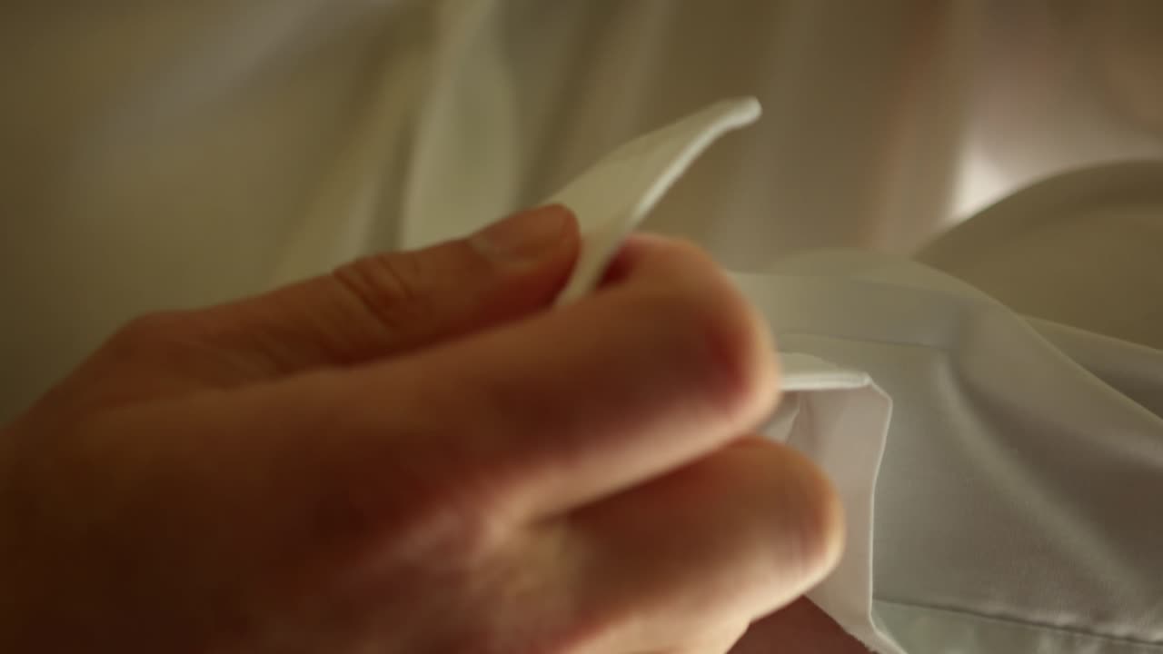 Close up handheld shot of groom putting cufflinks on white wedding shirt