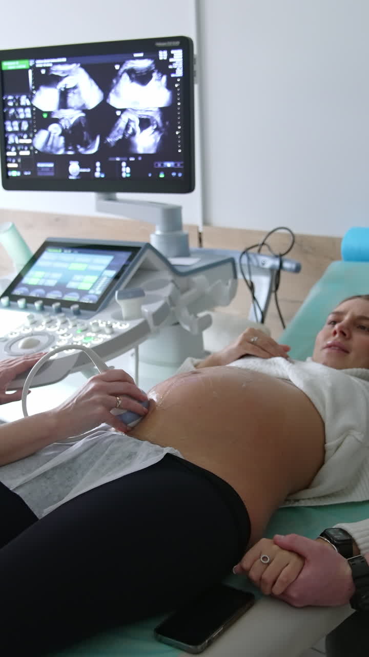 Young family couple at the ultrasound check. Doctor moves the sensor by the woman's belly and looks at the screen. Vertical video