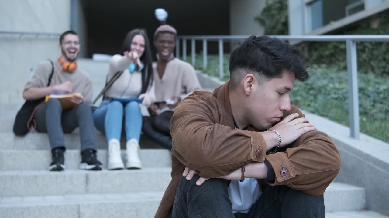 A group of students bulling an hispanic man sitting on the stairs outdoors
