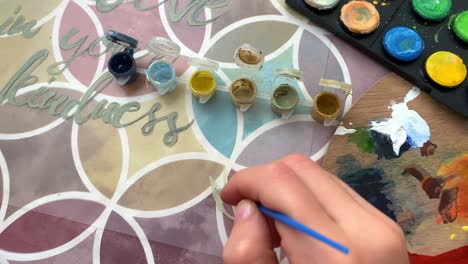 top down shot of a female hands painting leaves on a colrful canvas