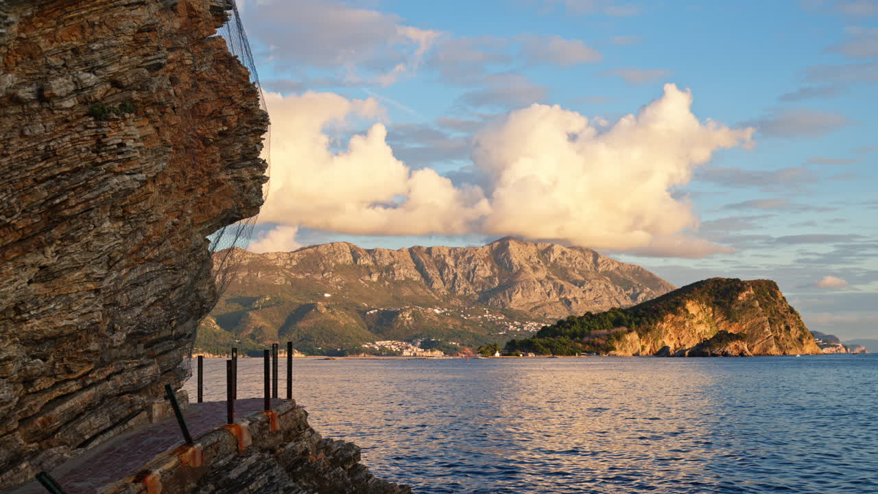 Sentiero stretto ricavato nella scogliera rocciosa a picco sul mare con isole e montagne sullo sfondo. Budva, Montenegro