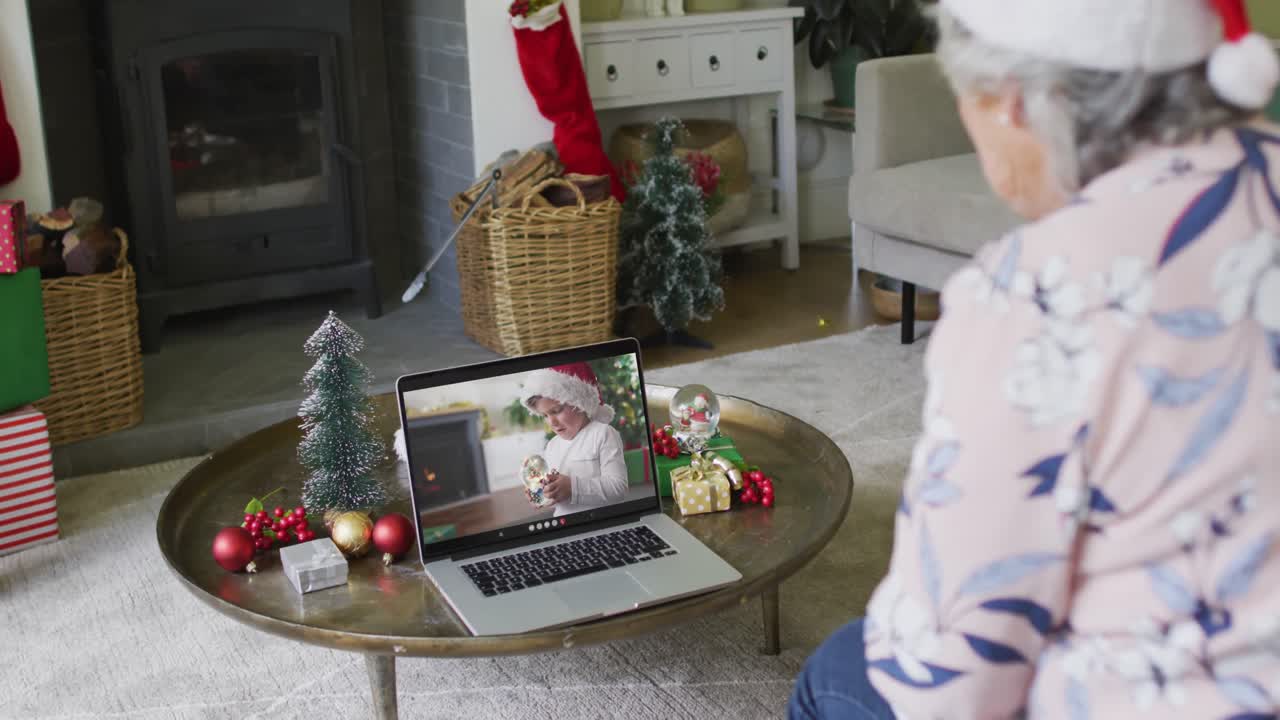mujer mayor caucásica con sombrero de santa usando una computadora portátil para una videollamada de navidad con un niño en la pantalla