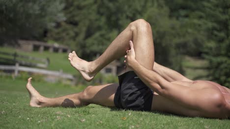 young caucasian fit attractive male exersicing outdoors hamstrings mobility exercise with green vegetation background slow motion 60 fps