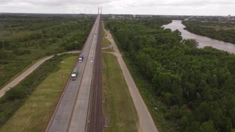 Aerial-shot-of-two-trucks-driving-on-Brazo-Largo-Bridge-beside-trees-and-river-in-Argentina