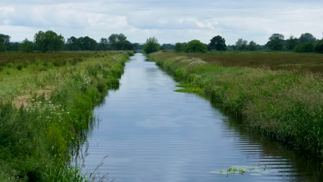 Scenic-landscape-view-of-long,-straight-drainage-river-flowing-through-green-fields-in-rural-countryside-on-the-Somerset-Levels-in-England-UK