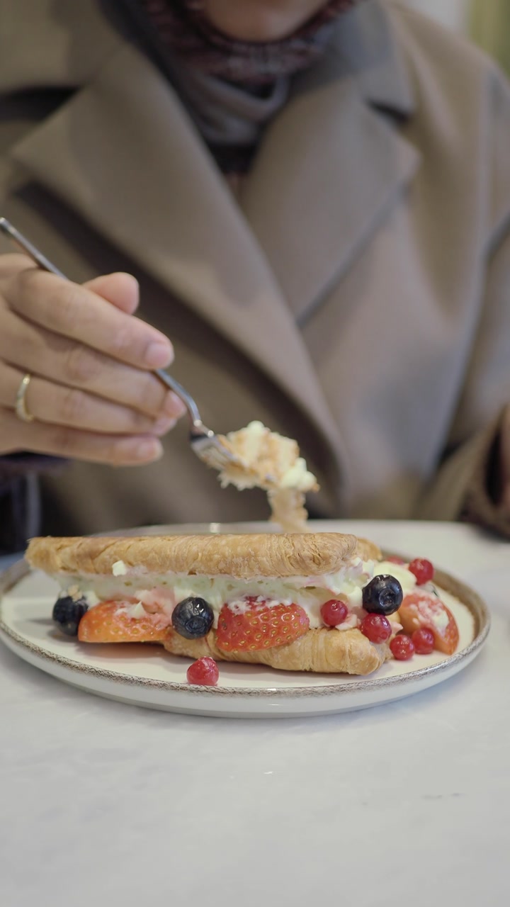 Close-up of a Woman Eating a Fruit Croissant with Berries and Cream