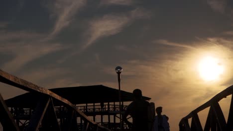 Un-Surfista-Masculino-Persigue-A-Sus-Amigos-En-El-Muelle-Al-Atardecer,-Toma-De-Seguimiento-En-Cámara-Lenta