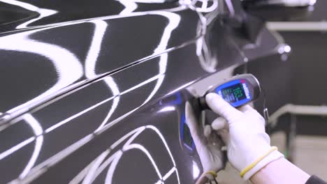 worker measures a thickness of primer on a car's body using a thickness gauge