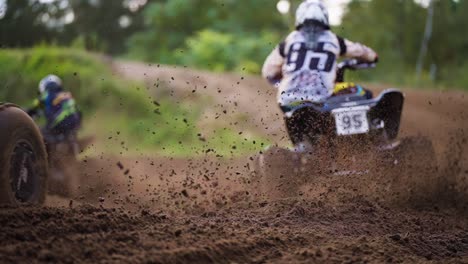 competencia de carreras de quads en camino fangoso de tierra con barro dispersándose bajo las ruedas en cámara lenta