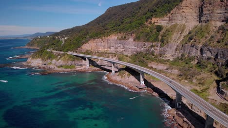 aerial view cars on sea cliff bridge, sunny day, grand pacific drive, new south wales, australia - dolly drone shot