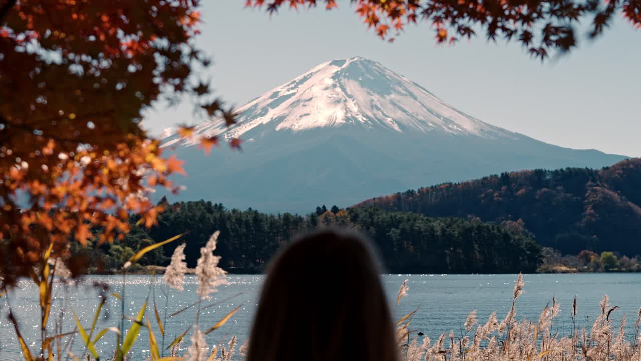 una serena toma de inclinación amplia que muestra la impresionante belleza del monte fuji desde el lago kawaguchiko en otoño y se ve a una mujer mirando el impresionante paisaje.