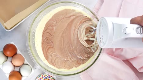 baking chocolate brownies and using a white electric mixer to mix the batter. making brownies on a white background surrounded by eggs, pink napkin and a baking pan. in the kitchen making a dessert